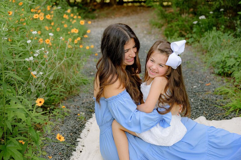 mother dressed in blue smiles as she looks at her daughter laughs