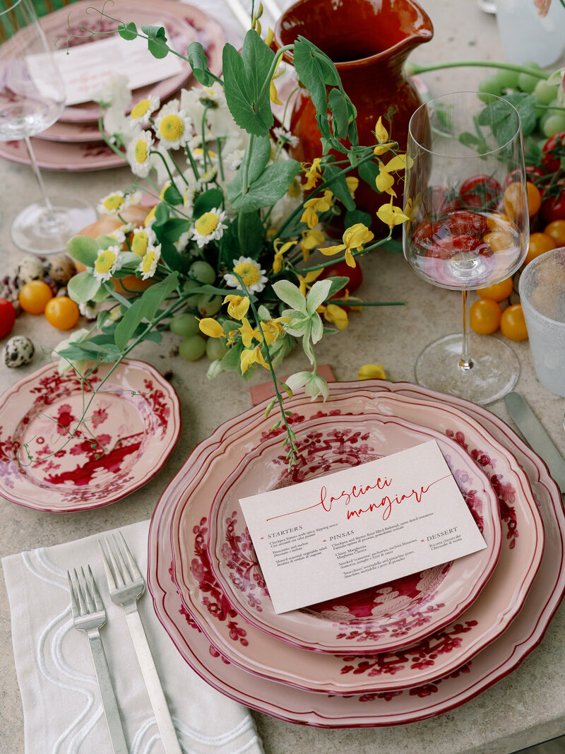 Welcome dinner design with red and pink hand painted Ginori plates, Tuscan vegetables, and yellow wildflowers