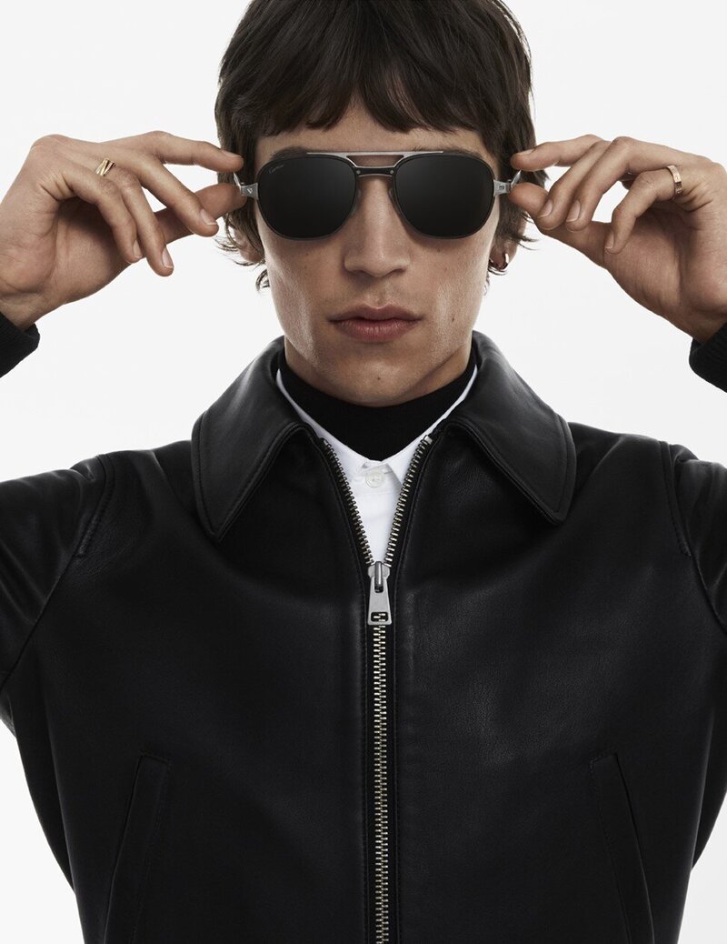 Close up shot of a man holding aviator sunglasses on his face wearing a leather jacket in front of a white background