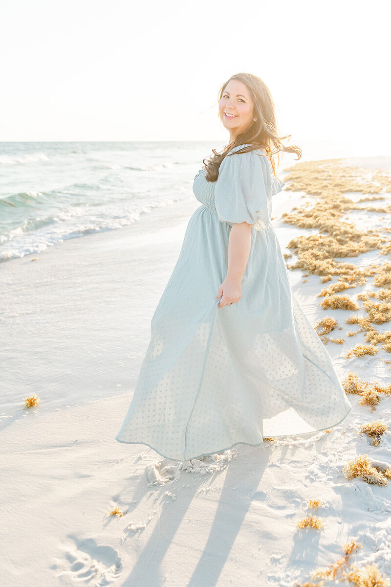 a pregnant woman happily dancing in front of the ocean, photographed by Destin maternity photographer