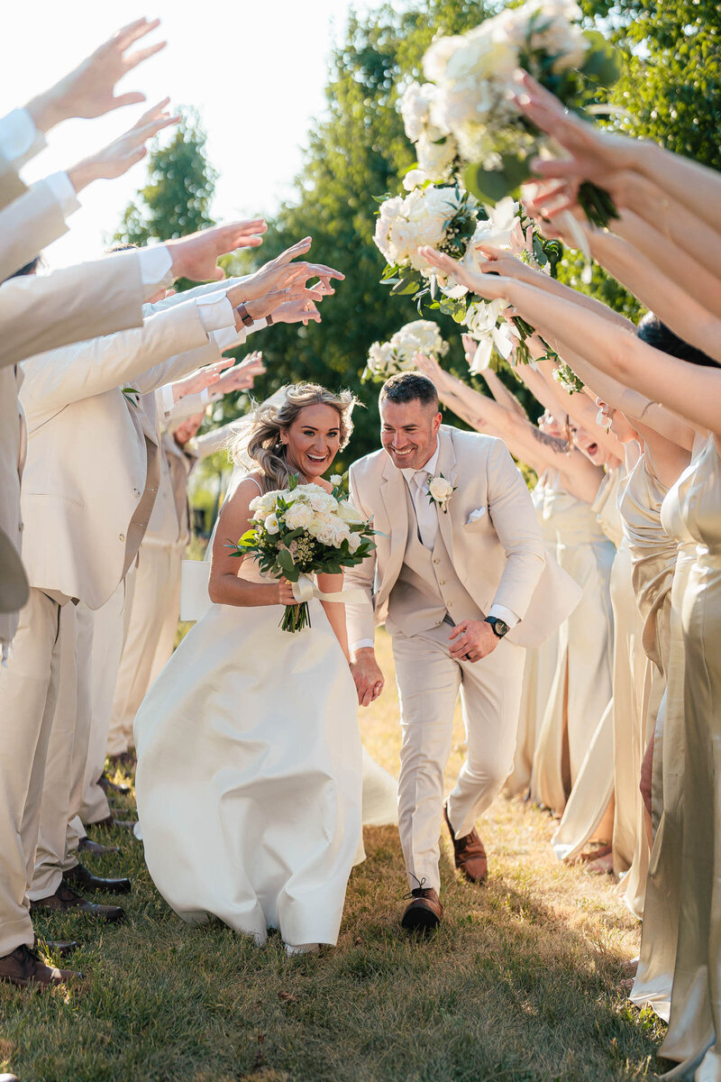 bride and groom run through tunnel of wedding party in the sunlight smiling big in columbus ohio