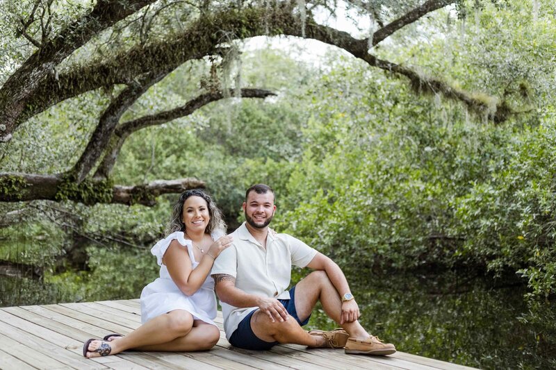 Man and woman sitting on dock in front of a sprawling live oak