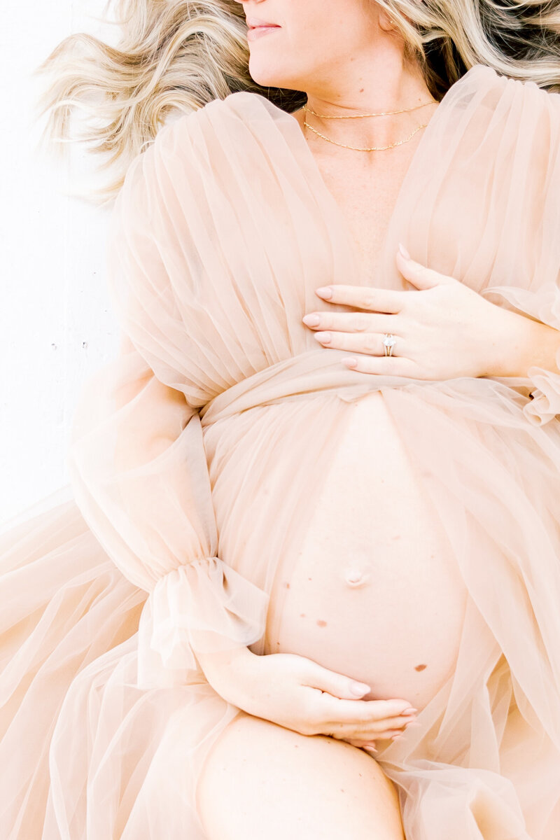 Details of a woman holding her bump while sitting in a studio