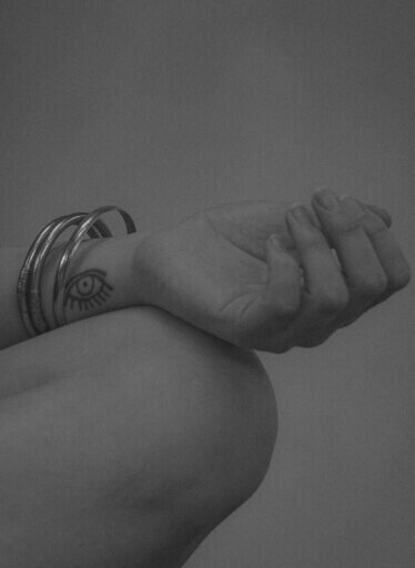 Close-up of a hand with an eye tattoo and bangles, symbolizing intuition and spiritual insight.