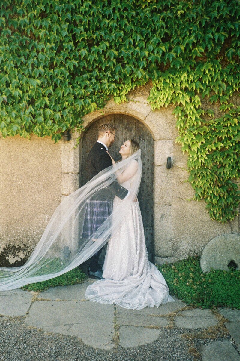 A bride and groom stand with their wedding party and smile for photography.  It is a 35mm film photograph.