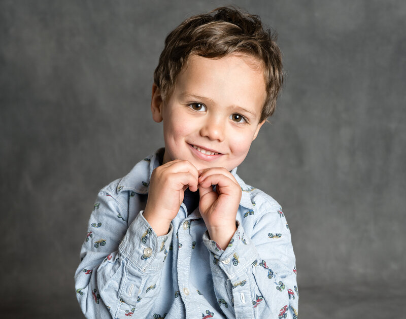 A child smiles with their hands together.