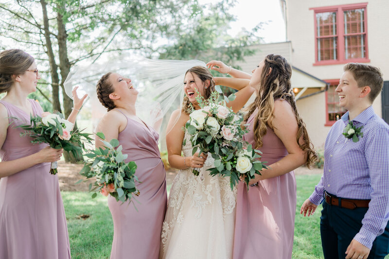 Bride and her wedding party laughing because the veil is flying over their faces