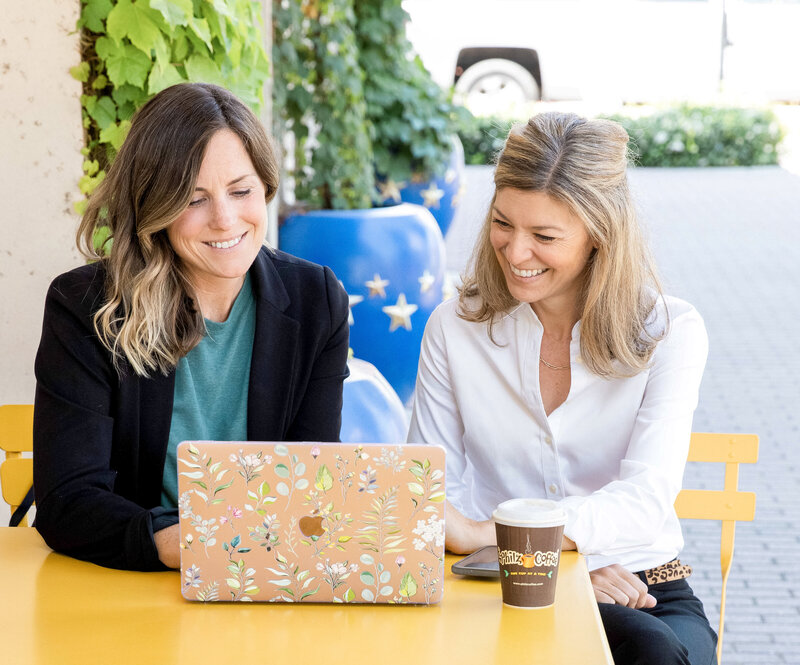 Two women working at outside cafe looking at laptop screen