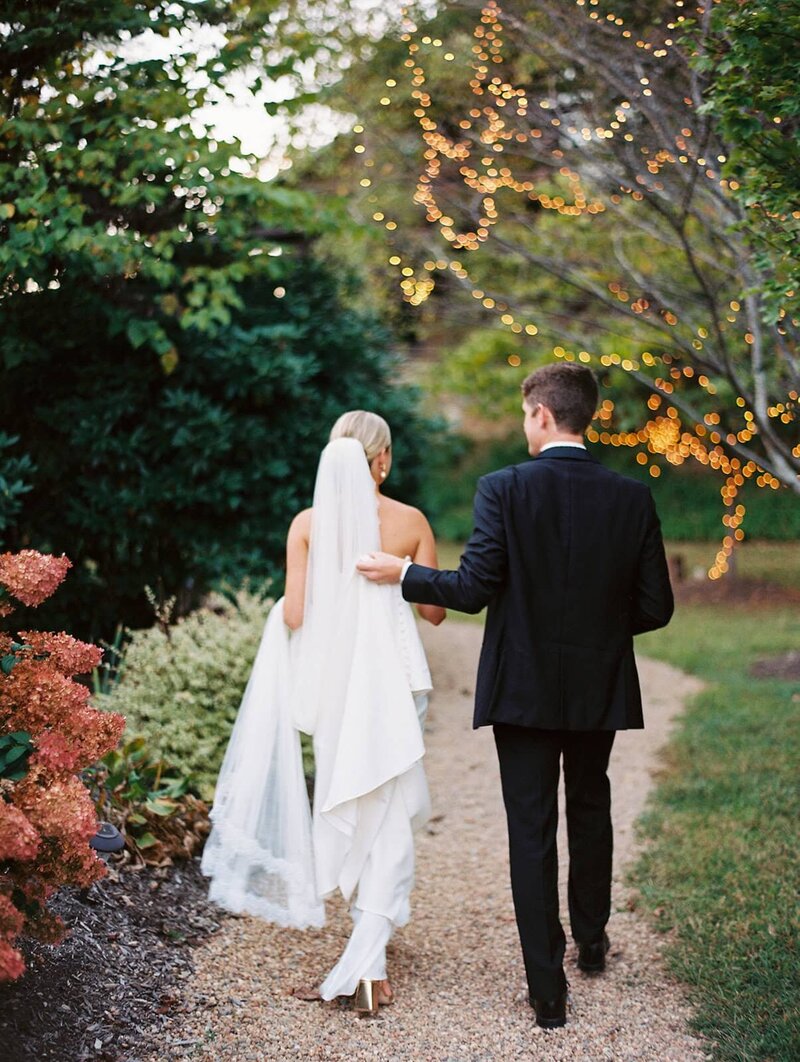 A bride and groom walk down a path at the Crest Center in Asheville, followed by Asheville Wedding Photographer Meghan Rose.