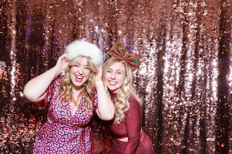 2 ladies posing against a champagne sequins backdrop, during