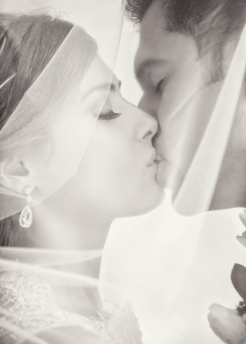 Bride and groom kissing under a veil