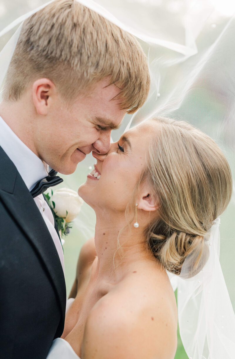 Bride and groom touching noses under the veil smiling at each other