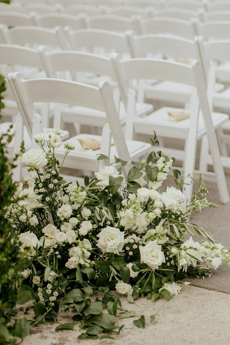 White floral aisle arrangement by ceremony chairs