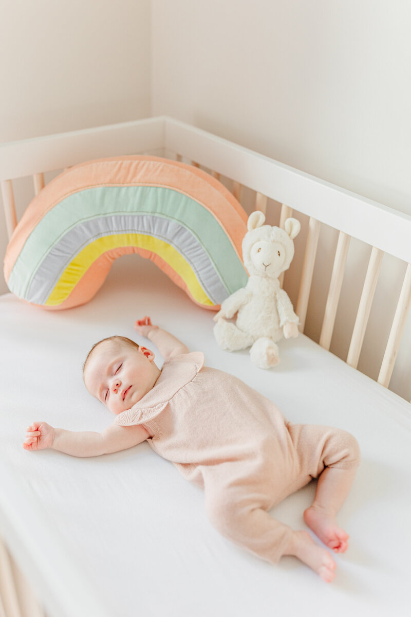 A baby wearing a pink onesie sleeps in her crib