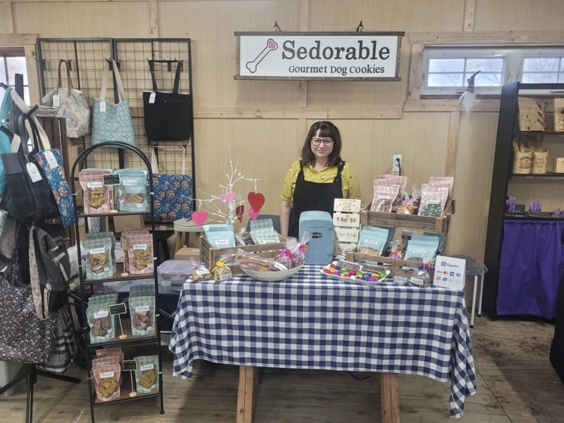 Jacqueline smiling at the Yarmouth Farmers’ Market stand with fresh dog treats on display.
