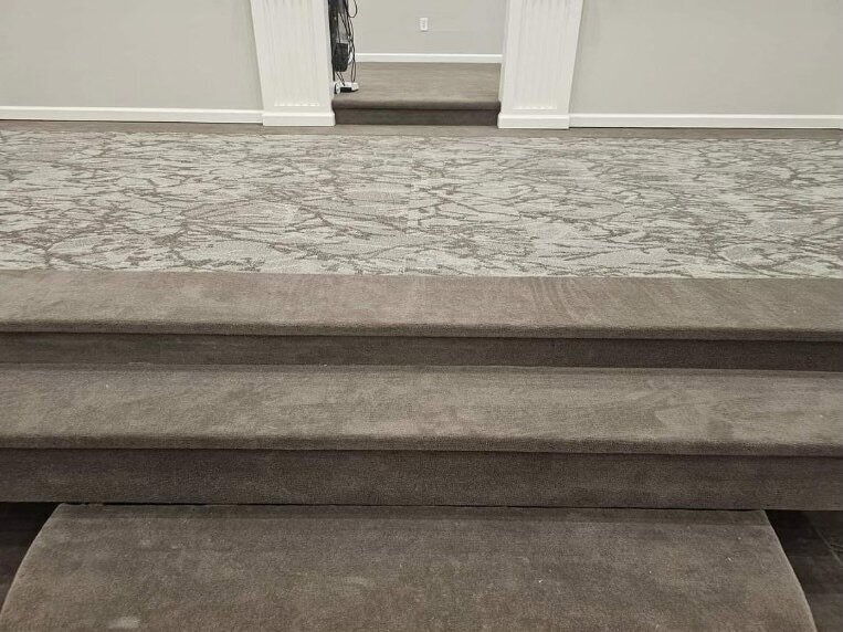 Closeup of stairs and light gray patterned carpet.