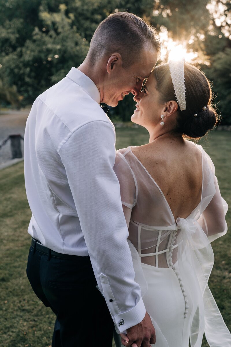 sunset shot of bride in haute sheer top with trish peng wedding dress and beaded headband and groom in white shirt with foreheads touching