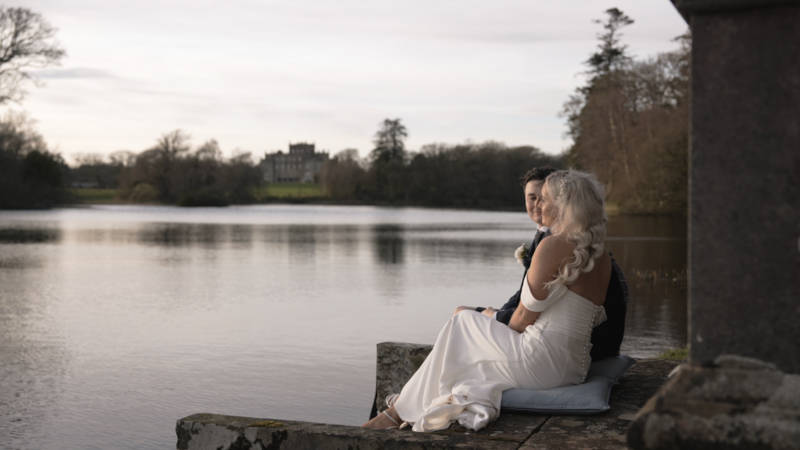 Couple sitting next to the water with Kinmount House in the background