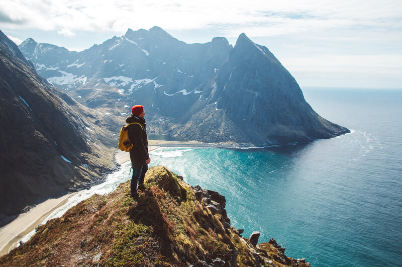 A hiker stands on a rocky ledge overlooking a stunning fjord, showcasing the beauty of nature and outdoor adventure.