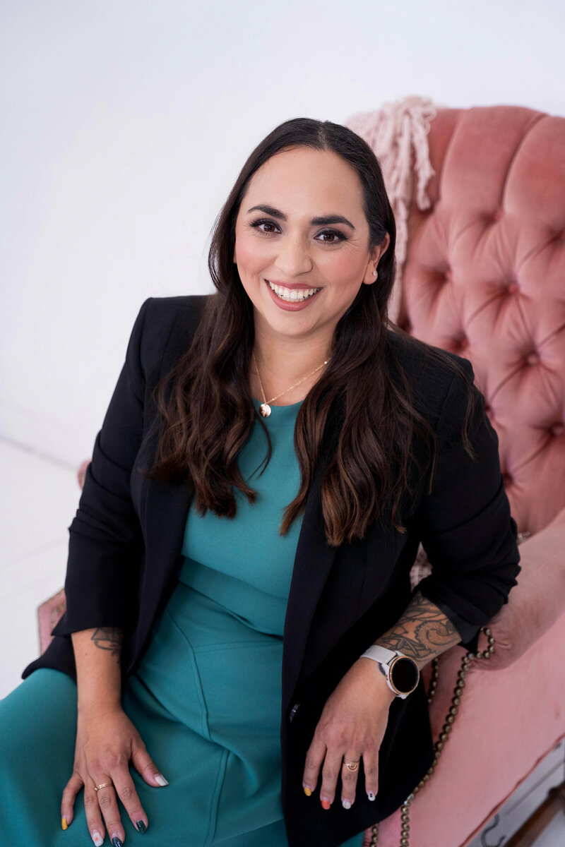 Stephanie, Founder of BCWise Consulting, in a blazer sitting on a pink chair 