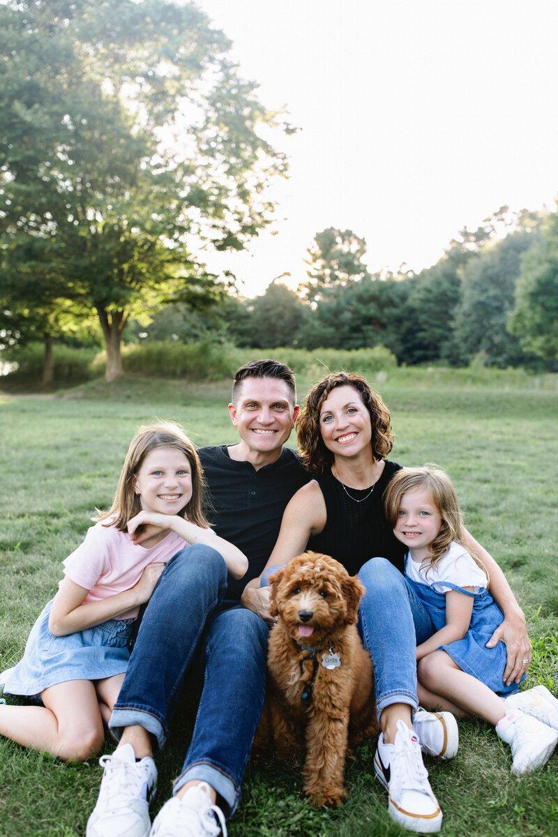 family of 4 plus dog posing for picture sitting on a blanket in a field