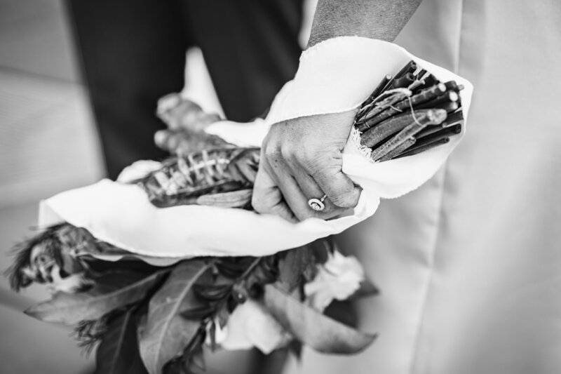 black and white close up of bride's hand clutching bridal bouquet with stems wrapped in fabric, the ring appears to be vintage.