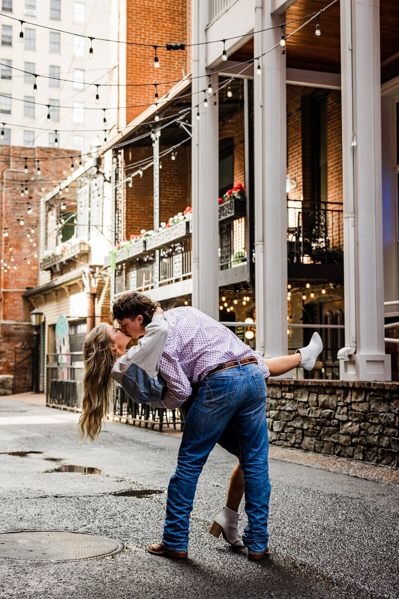 Man dipping his fiance while kissing her in front of a brick building