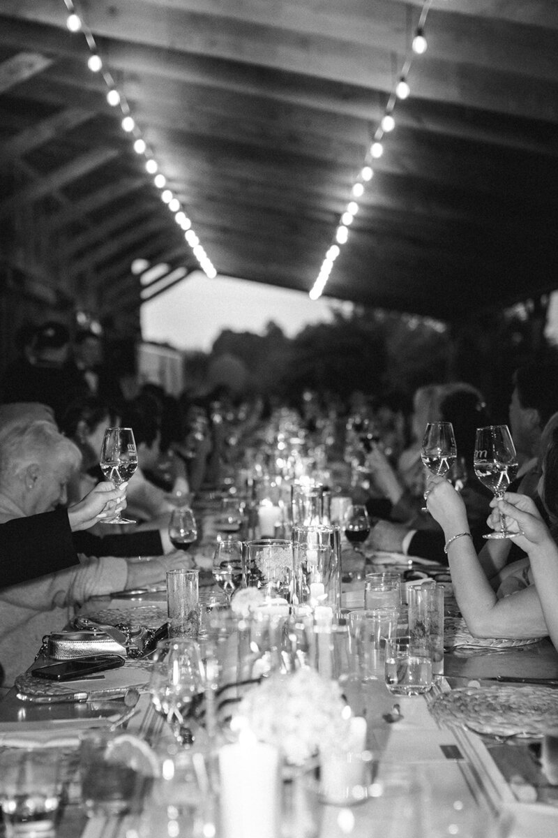 A black and white long-table dinner setting under string lights at an outdoor venue.