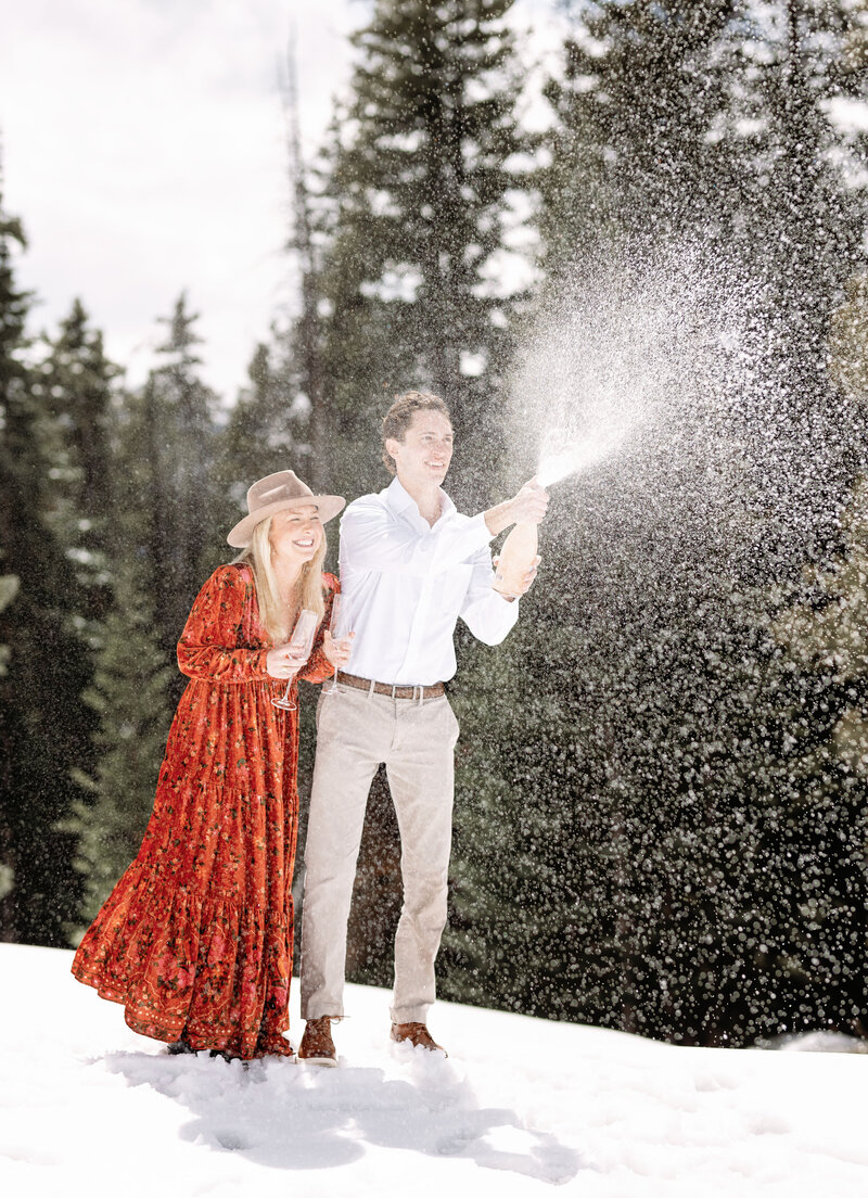 A couple sprays champagne into the air laughing and enjoying the moment after their engagement