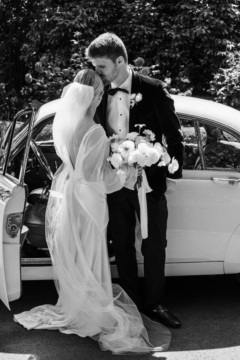 black and white photo of a couple in front of vintage white car after their christchurch wedding