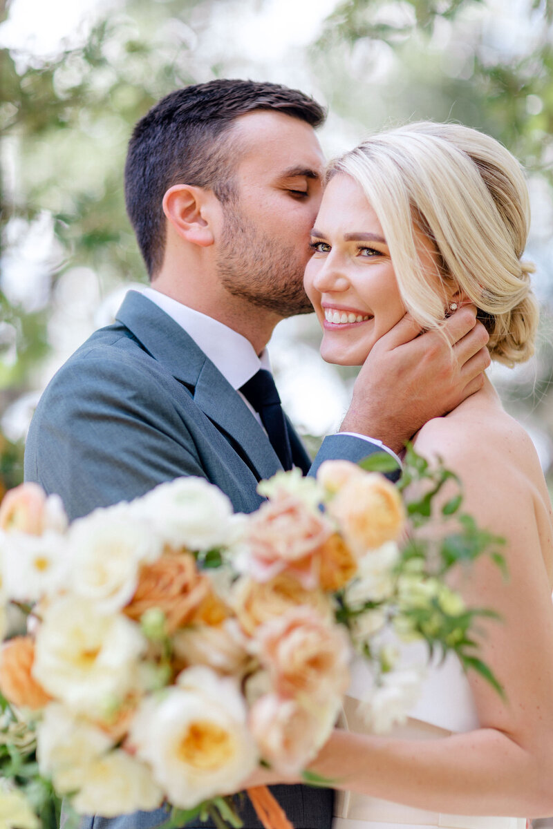 Groom kisses the side of bride's face at the wayback