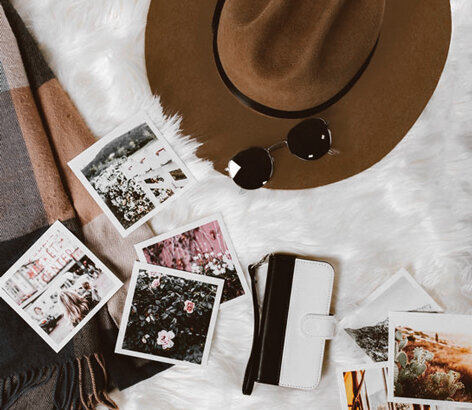 polaroid images, hat, and sunglasses scattered on a blanket