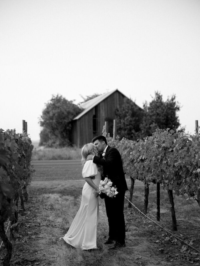 bride and groom share a kiss in vineyards at abeja winery