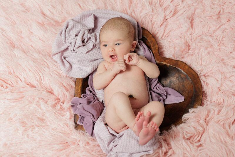 A baby laying on a wooden heart and purple blanket