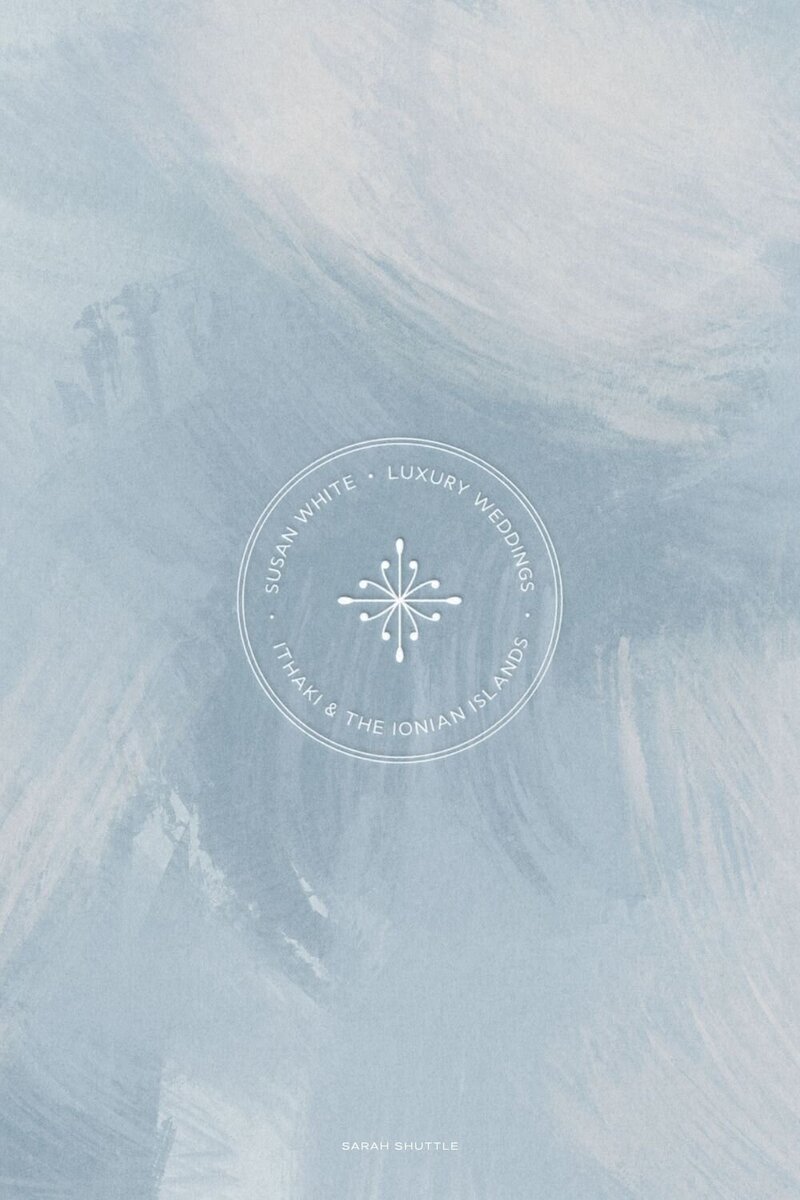 Elegant emblem design for destination wedding planner Susan White Luxury Weddings, displayed on a blue painted pattern reflecting the Greek islands.