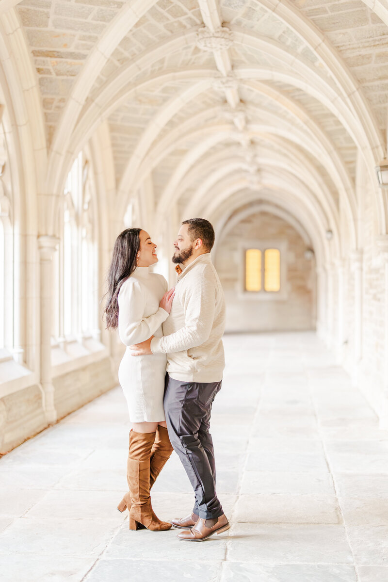 A newly engaged couple shares an intimate moment in an ornate hallway in cream outfits