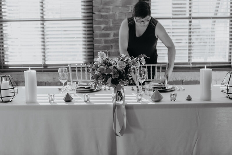 Black and white photo of a person arranging a table with floral centerpiece.