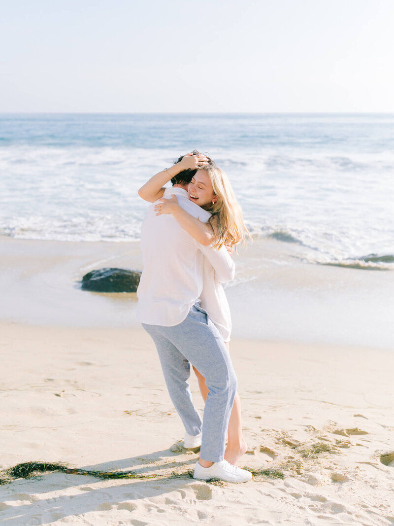 beach engagement photo of couple hugging with ocean background