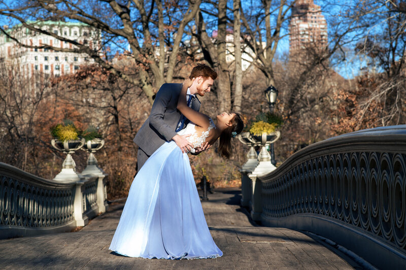 Young wedding couple enjoying an embrace in Central Park's Bow Bridge.  Bride wears blue gown.