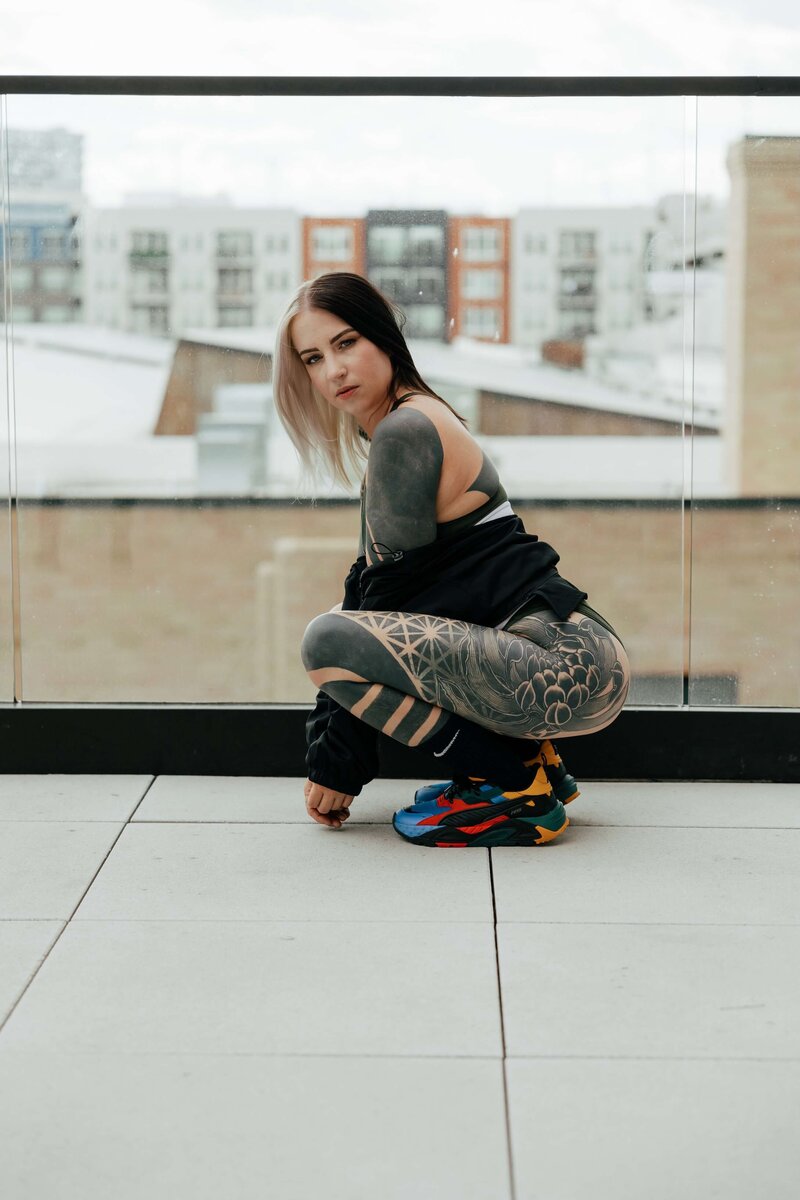 Tattooed Woman Squatting on Balcony With Colorful Sneakers