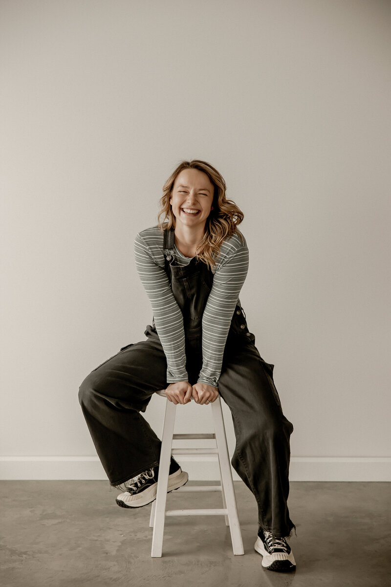 Amber sitting and gripping the  stool while smiling at the camera