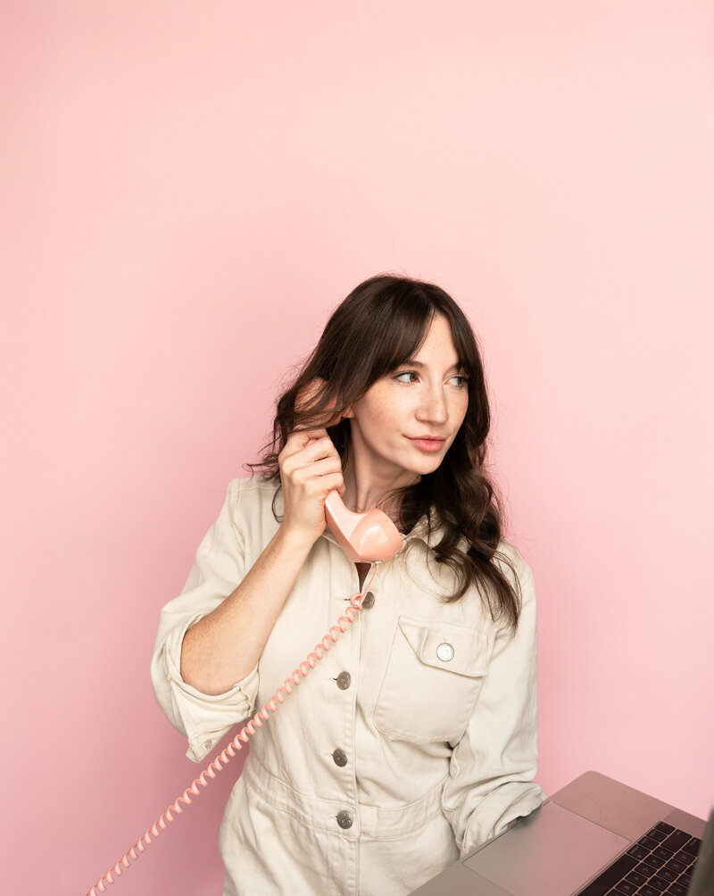 Woman holding pink phone and laptop.
