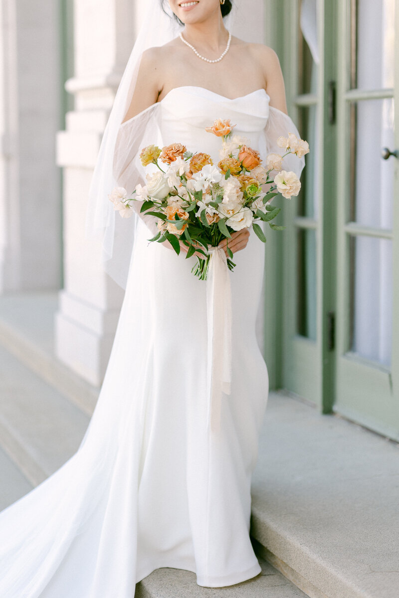 Close up of beautiful bride holding a white and orange floral bouquet