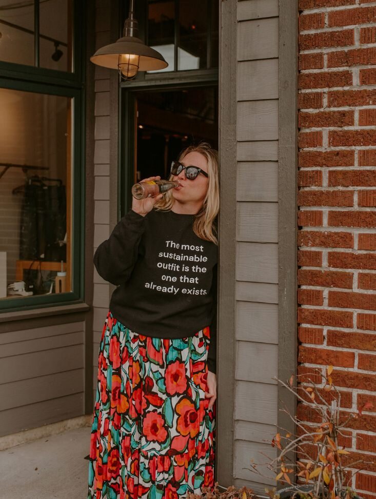 A person leaning against a wall drinking from a glass bottle 