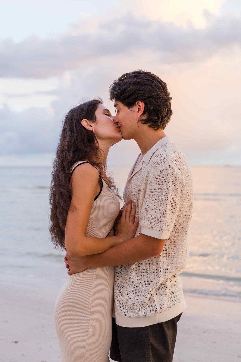 Couple kisses with blue and pink ocean sunset behind them