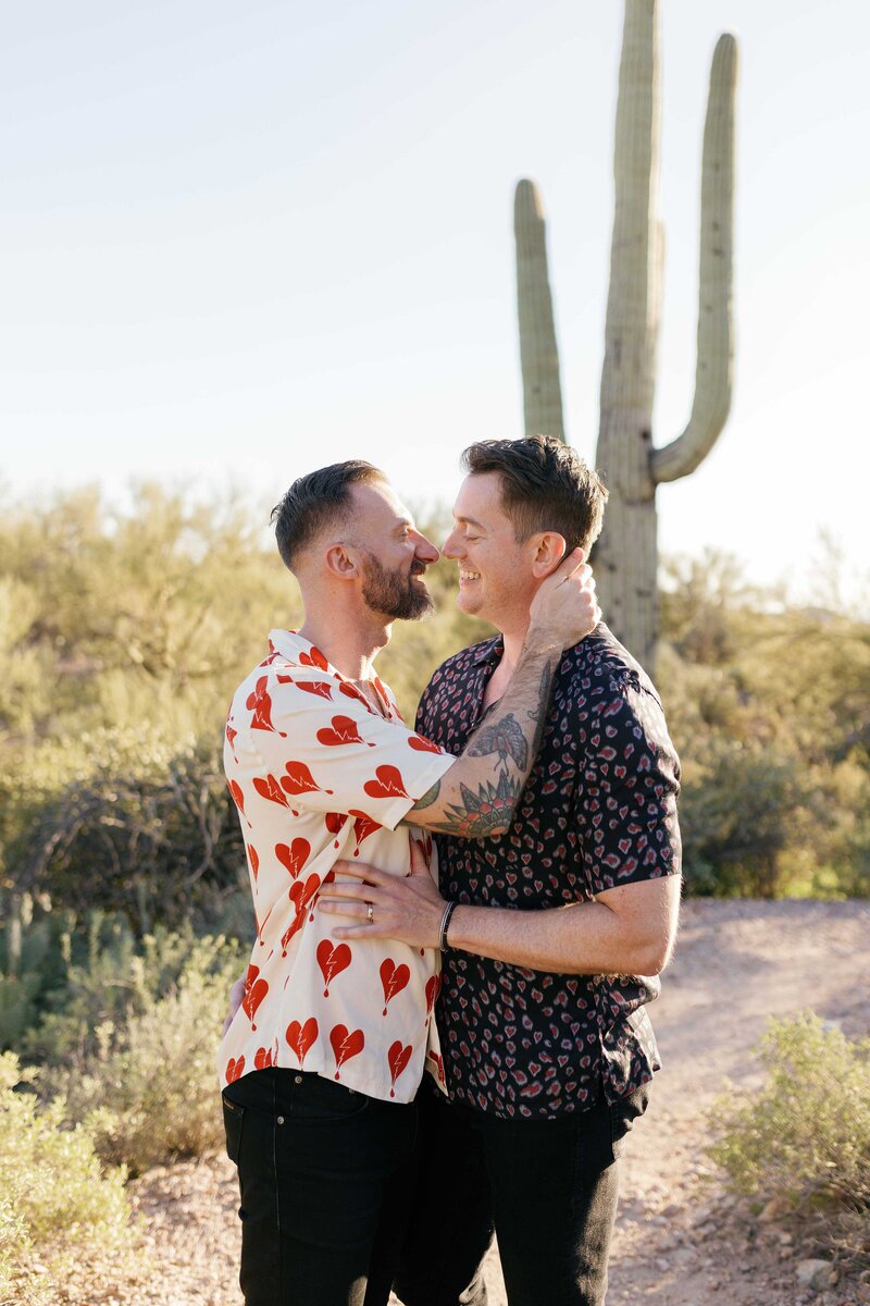 Two grooms cuddle in the desert for their engagement photos.