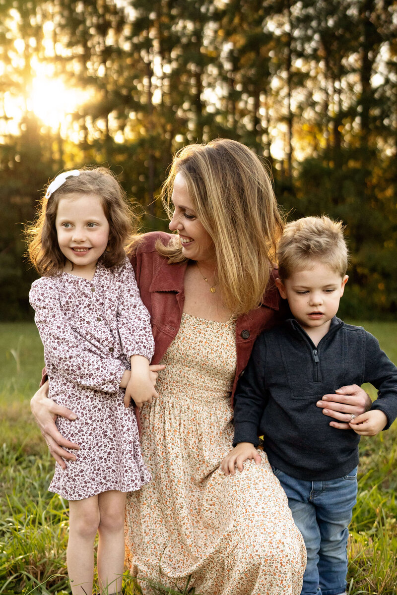 Mother kneeling in grass with young son and daughter during sunset