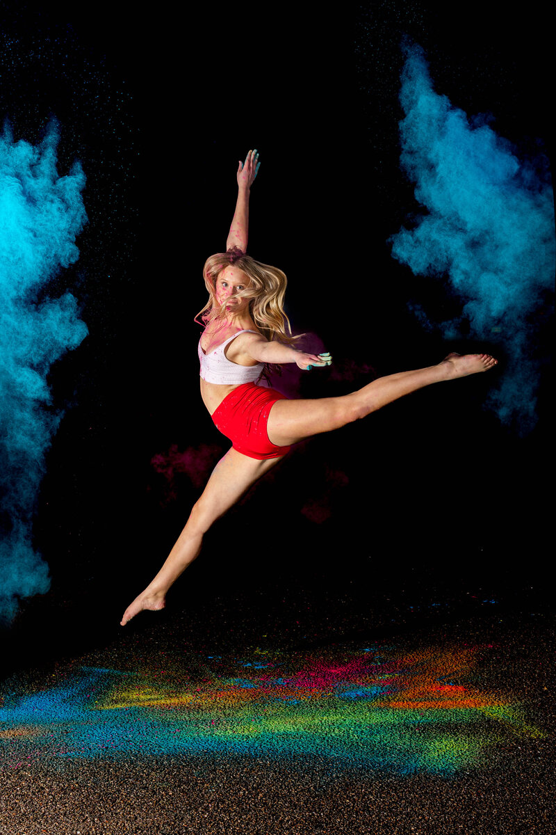Dynamic midair leap captured by Brooke Tucker during a Color + Motion powder session, with vibrant blue and rainbow powder highlighting a dancer's strength and grace