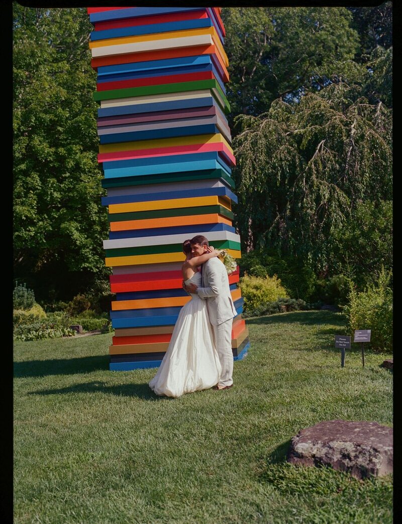 Intimate Brooklyn wedding couple embracing beside a colorful outdoor art installation, captured in a candid documentary wedding photography style