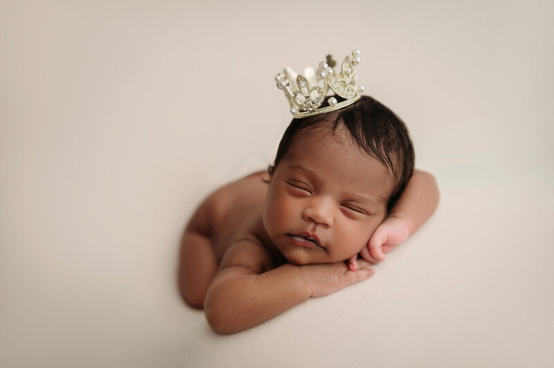 Sleeping baby girl wearing a princess crown in front of beige backdrop photographed by Drea S Photo in Connecticut Studio